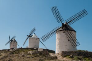 Whitewashed windmills with wooden lattice sails standing along the ridge above Consuegra, under a clear blue sky.