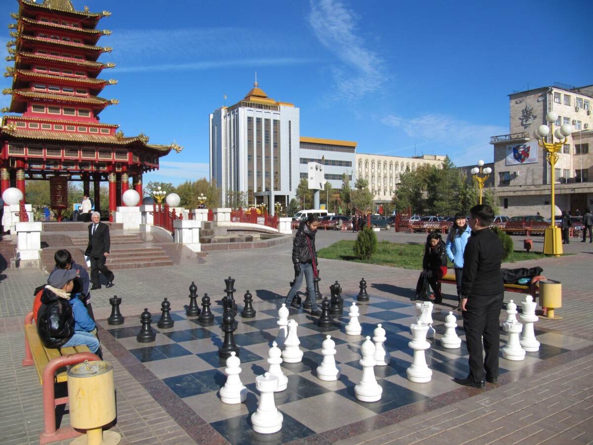 A giant outdoor chess set fills a plaza in Elista, with players moving oversized pieces in front of a red and gold pagoda gate.