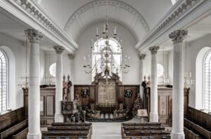 The white columned interior of the rebuilt Wren church in Fulton, Missouri, with chandeliers, wooden pews and an altar decorated for Christmas.