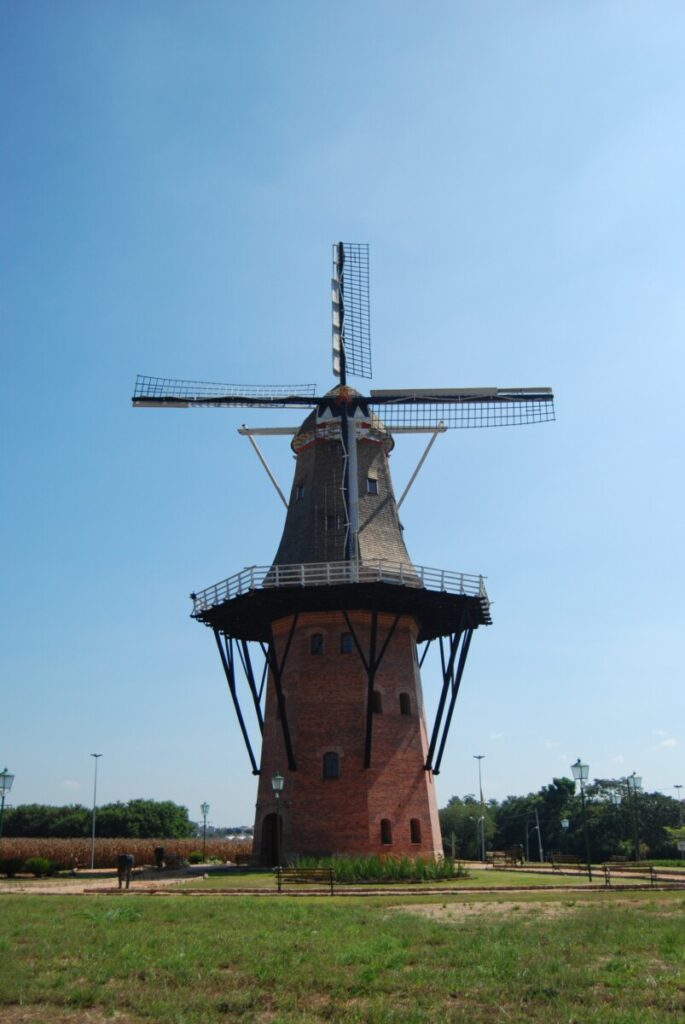 The brick Moinho Povos Unidos windmill in Holambra, its lattice sails spread against a clear blue sky above open fields.