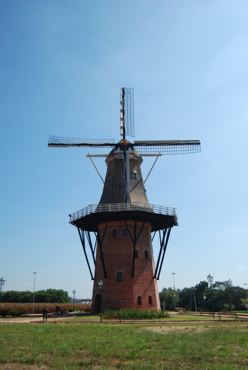 The brick Moinho Povos Unidos windmill in Holambra, its lattice sails spread against a clear blue sky above open fields.