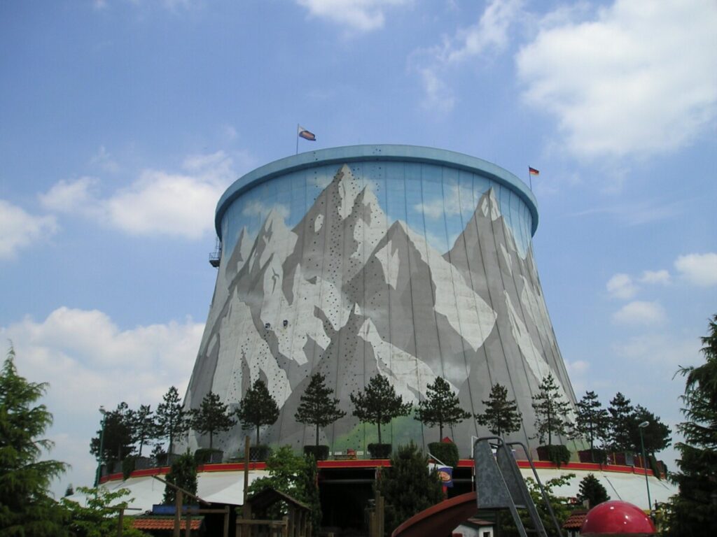 The cooling tower of the former Kalkar nuclear plant, now part of the Wunderland Kalkar theme park, rising over swing rides and roller coasters.