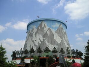 The cooling tower of the former Kalkar nuclear plant, now part of the Wunderland Kalkar theme park, rising over swing rides and roller coasters.