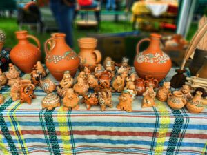 A market table at an Opishnia pottery festival, covered with an embroidered Ukrainian cloth and lined with painted clay jugs, pitchers and whimsical animal figurines.