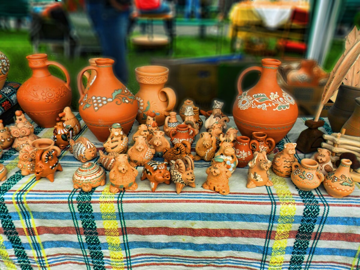 A market table at an Opishnia pottery festival, covered with an embroidered Ukrainian cloth and lined with painted clay jugs, pitchers and whimsical animal figurines.