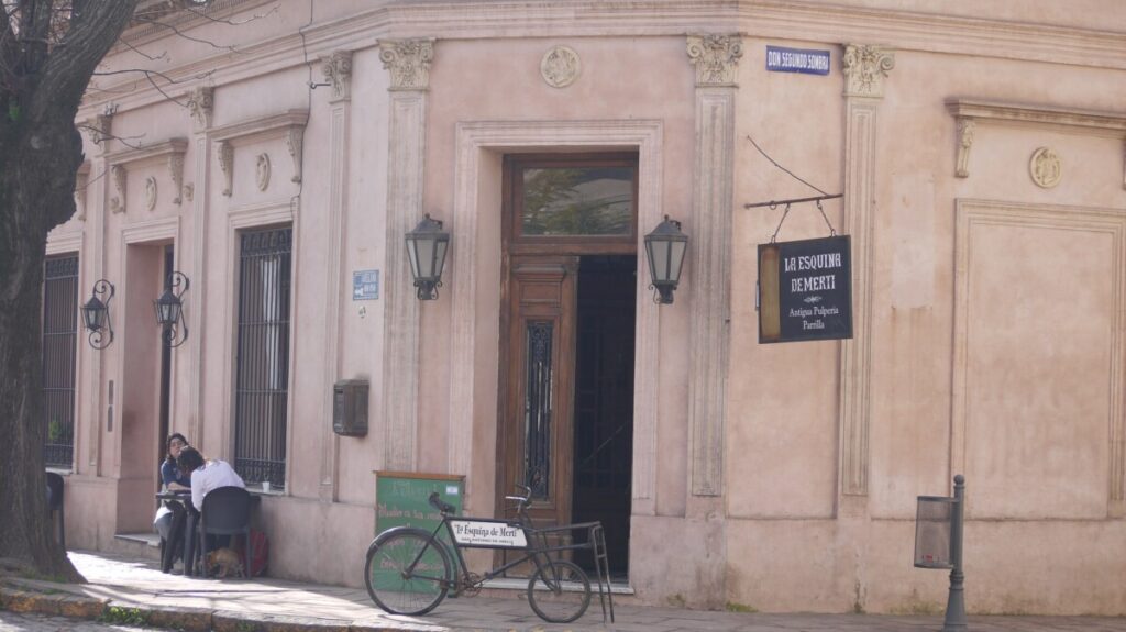 A pink corner building on Don Segundo Sombra street in San Antonio de Areco, the old pulpería La Esquina de Merti, with hanging lanterns and a bicycle parked outside.