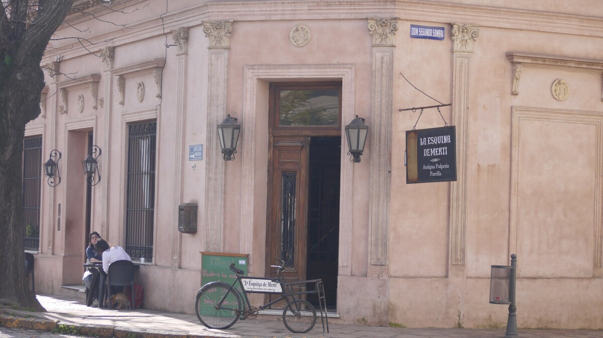 A pink corner building on Don Segundo Sombra street in San Antonio de Areco, the old pulpería La Esquina de Merti, with hanging lanterns and a bicycle parked outside.