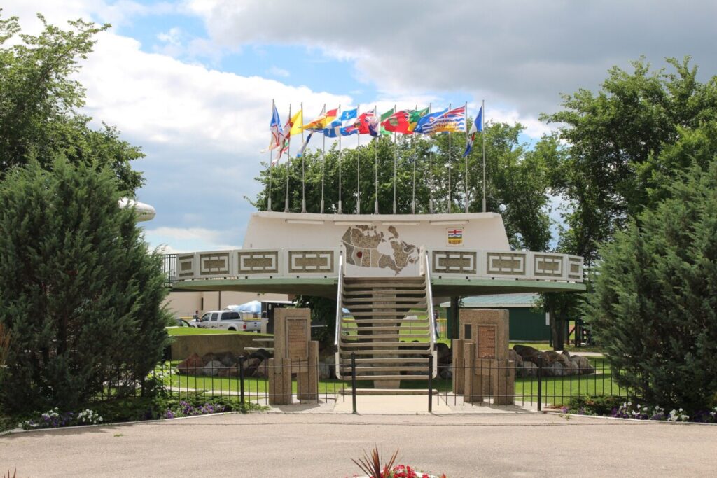 The saucer-shaped UFO landing pad in St. Paul, Alberta, its rail hung with the flags of Canada's provinces and territories, above a stone map of Canada.