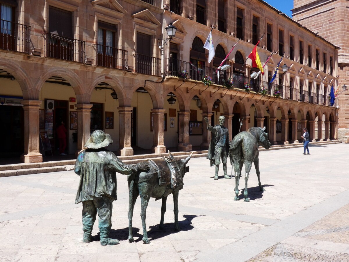 Bronze statues of Don Quixote and Sancho Panza with their horse and donkey in the arcaded Plaza Mayor of Villanueva de los Infantes.