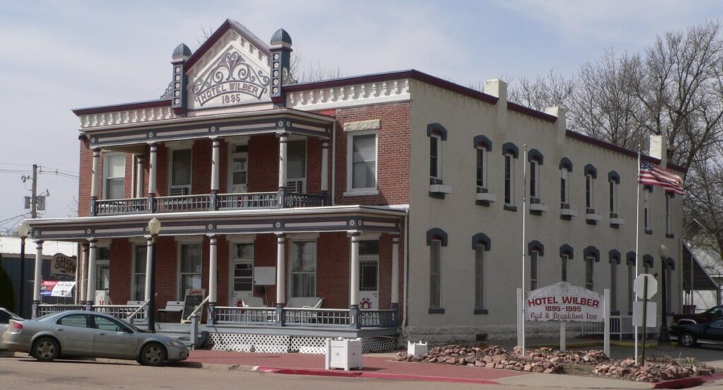 The two storey brick Hotel Wilber, built in 1895, with stacked porches, an American flag and a sign reading Hotel Wilber Bed and Breakfast Inn.